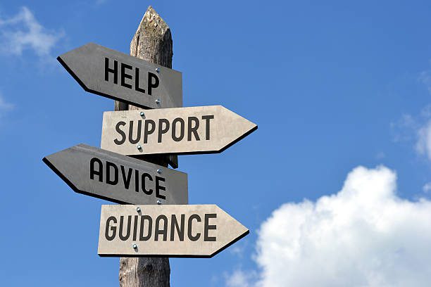 Wooden singpost with "help, support, advice, guidance" arrows against blue sky.